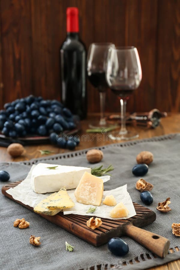 Placa de madeira com tipos diferentes de queijo, de uvas maduras e de porcas na tabela imagem de stock Placa de madeira com tipos diferentes de queijo, de uvas maduras e de porcas na tabela imagem de stock