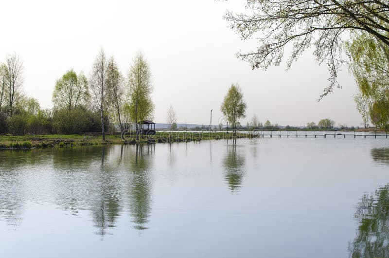 A place for meditation-wooden gazebo stands on the shore of the Lake near the young trees. Spring background forest green nature outdoor park pond water arbor garden house landscape river tourism architecture autumn bbq calm cold color dark day europe fantasy fishing fog foggy foliage light outdoors panorama peaceful picnic rain rainy recreation season shed shop sun sunlight vacation weather wet woods beauty natural reflection travel environment beautiful blue bridge building grass pavilion plant romantic sky summer tranquil view walk wedding