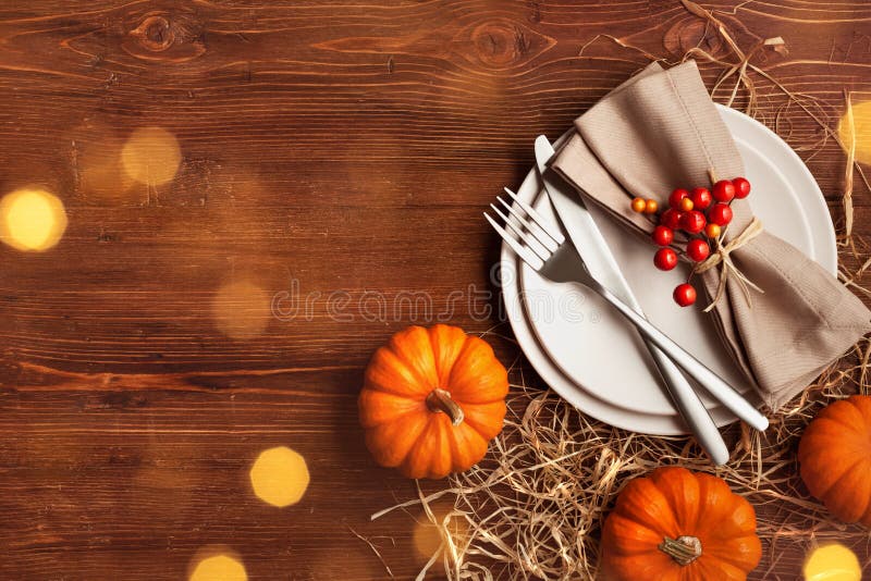 Place setting for Thanksgiving dinner with plate, napkin, cutlery and pumpkins on wooden table top view