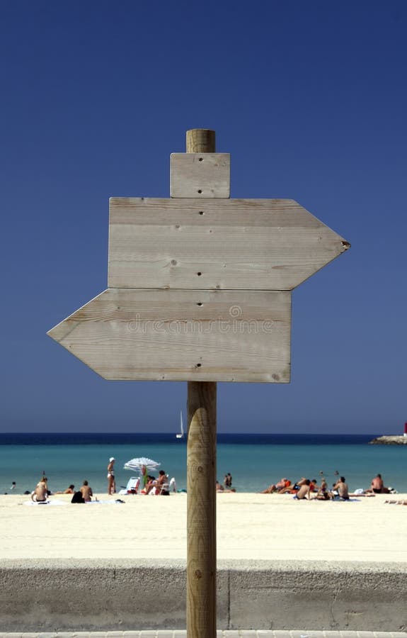 A view of the white sands and blue water along El Arenal beach on the Spanish island of Majorca or Mallorca. Wooden sign post is in the foreground. A view of the white sands and blue water along El Arenal beach on the Spanish island of Majorca or Mallorca. Wooden sign post is in the foreground.