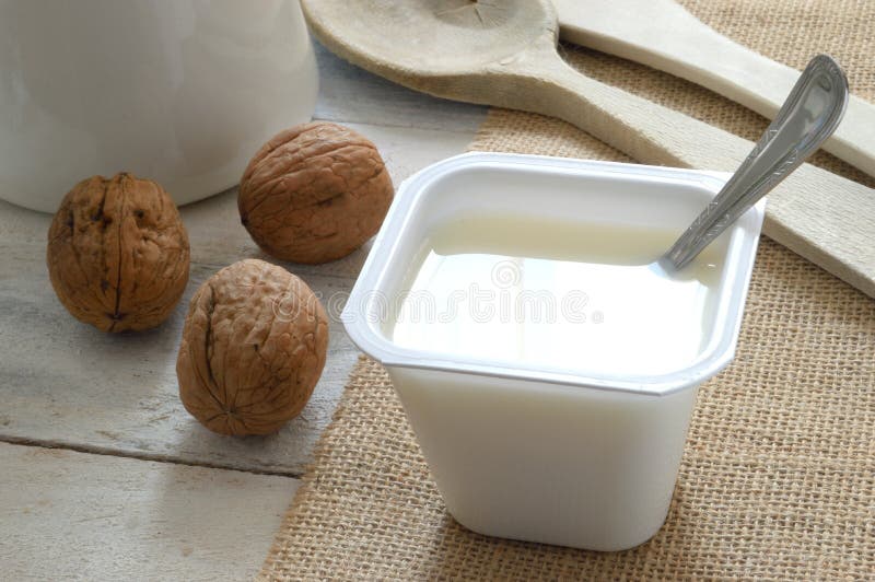 Plain yogurt on a sack cloth with some nuts served in a wooden white table of a rustic kitchen.