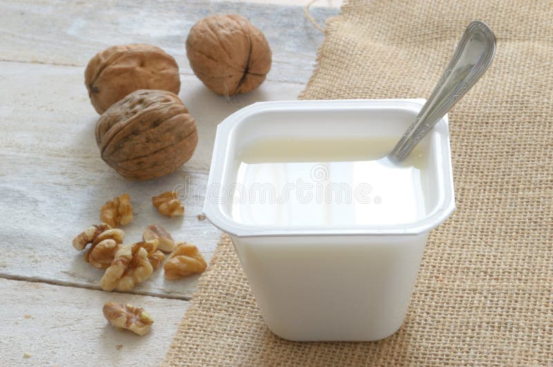 Plain yogurt on a sack cloth with some nuts served in a wooden white table of a rustic kitchen.