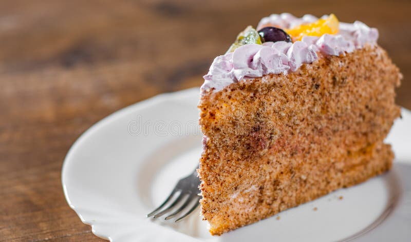 Plak van gelaagde Verjaardagscake met room met fruit in een plaat op houten royalty-vrije stock fotografie Plak van gelaagde Verjaardagscake met room met fruit in een plaat op houten royalty-vrije stock fotografie