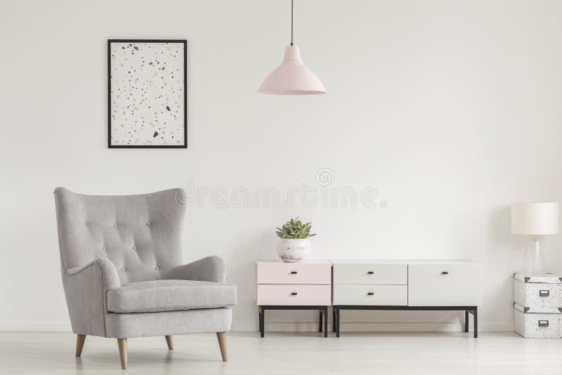 Plakat über grauem Lehnsessel und Lampe in weißem Wohnzimmer interio