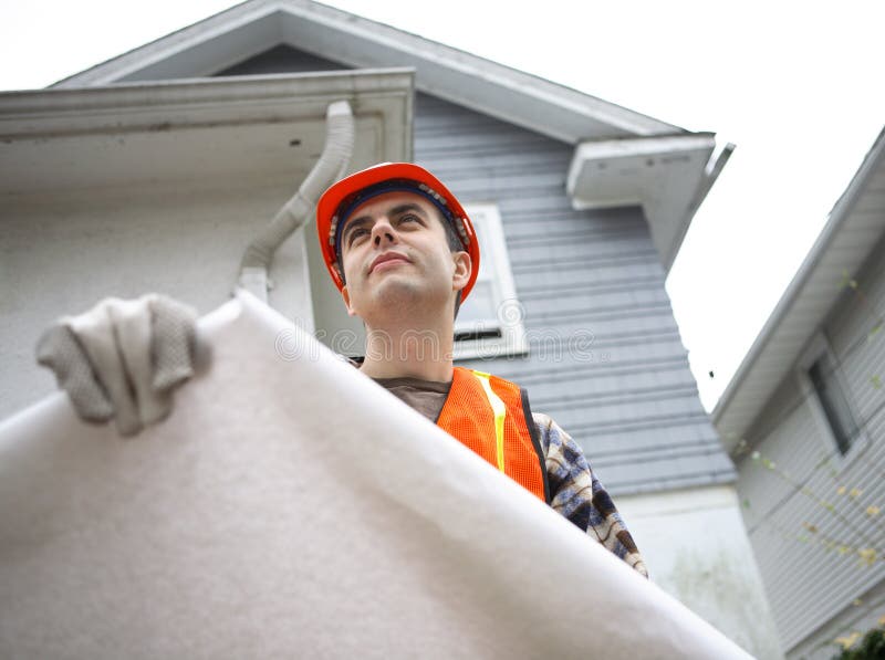 Construction worker holding blueprints. Residential house in the background. Architect uniform stock images, royalty-free photos and pictures