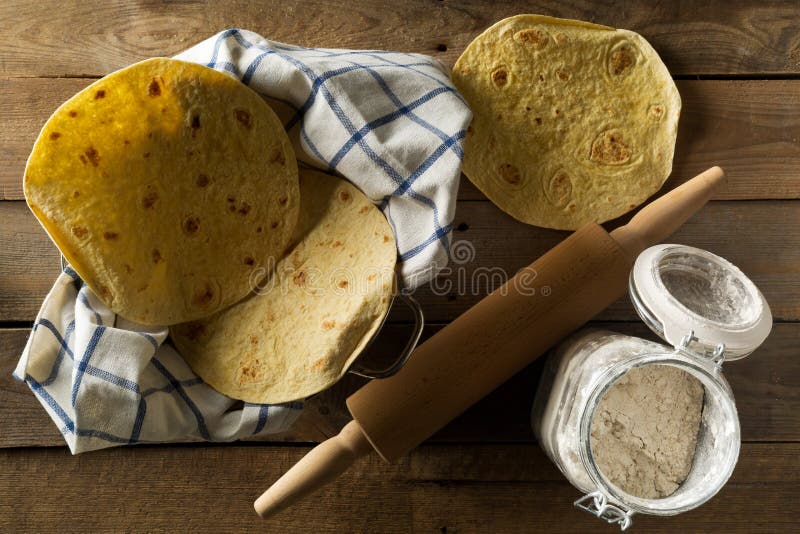 Plan lekmanna- bästa sikt för ny tom vetetortilla på disktrasan på den lantliga trätabellen med mjöl och kavel arkivbilder Plan lekmanna- bästa sikt för ny tom vetetortilla på disktrasan på den lantliga trätabellen med mjöl och kavel arkivbilder