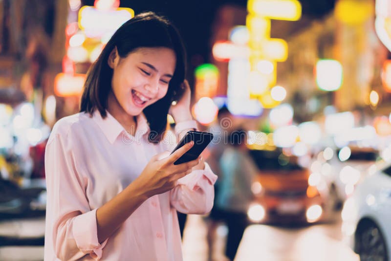 Plan rapproch? de femme tenant un smartphone la nuit sur la rue d'achats de ville, et la promenade de personnes photo stock Plan rapproch? de femme tenant un smartphone la nuit sur la rue d'achats de ville, et la promenade de personnes photo stock