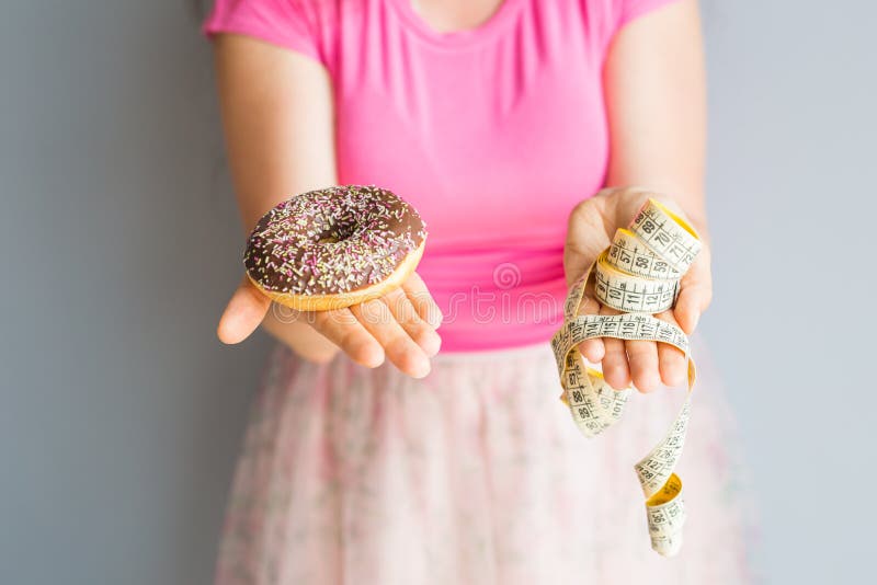 Plan rapproché des mains du ` s de femme tenant un beignet et une bande de mesure Le concept de la consommation saine Régime photos libres de droits Plan rapproché des mains du ` s de femme tenant un beignet et une bande de mesure Le concept de la consommation saine Régime photos libres de droits