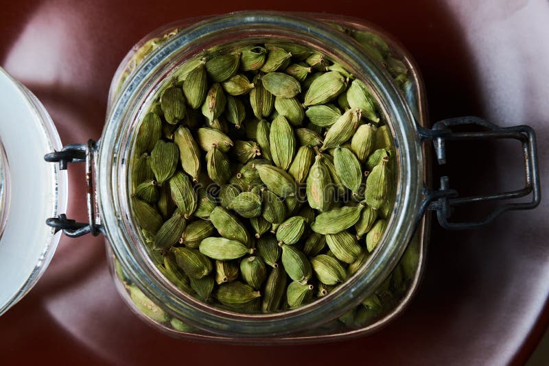 Plan rapproché proto du pot en verre complètement de cosses vertes de cardamome de plat brun photos libres de droits Plan rapproché proto du pot en verre complètement de cosses vertes de cardamome de plat brun photos libres de droits