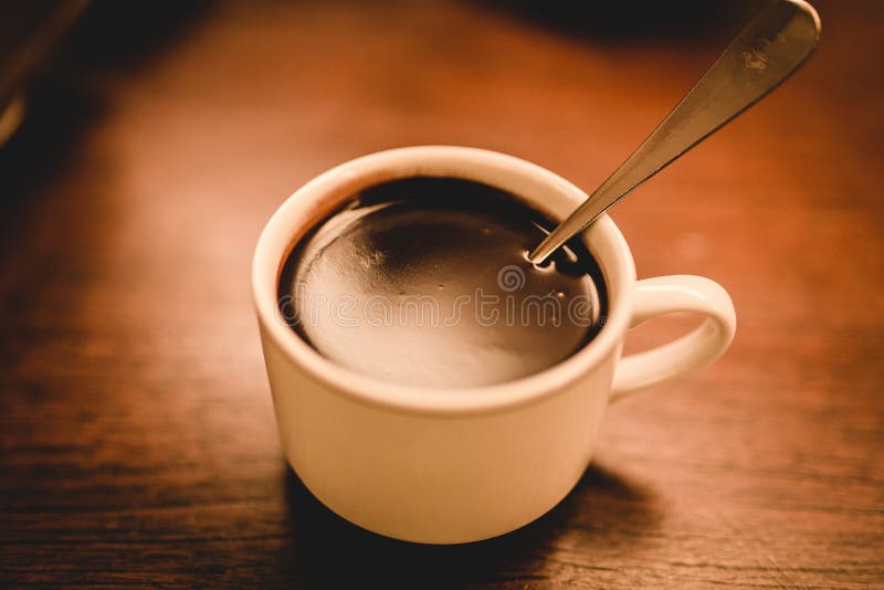 Plan rapproché tiré de la tasse en céramique blanche d'expresso remplie du café sur la surface en bois brune photos stock Plan rapproché tiré de la tasse en céramique blanche d'expresso remplie du café sur la surface en bois brune photos stock