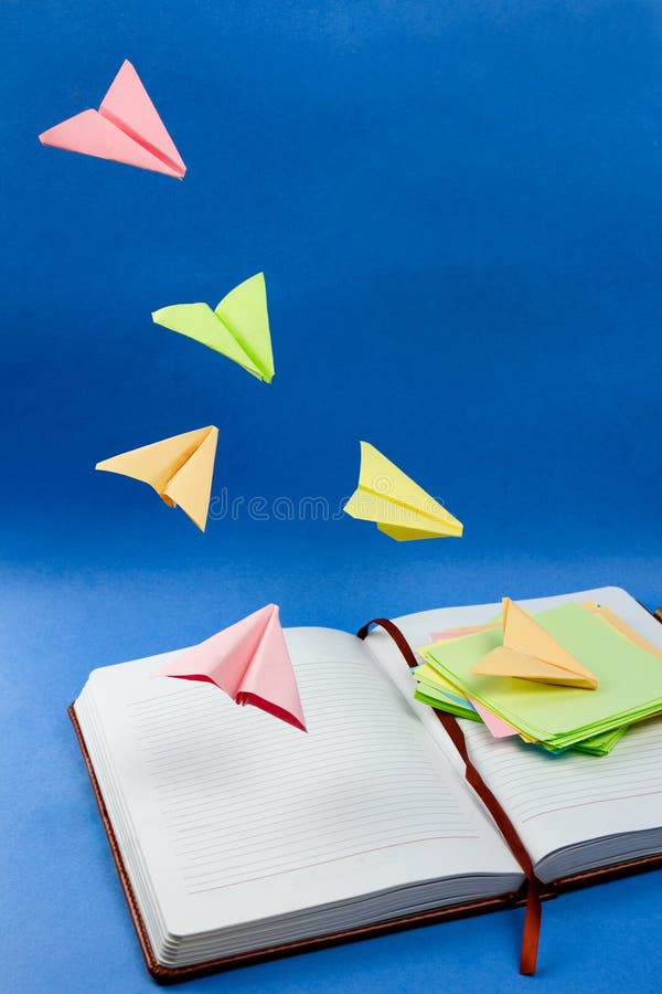Planes made from colorful note papers flying over the notebook. royalty free stock image Planes made from colorful note papers flying over the notebook. royalty free stock image