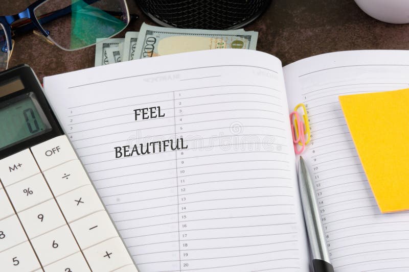A planner opened to a page displaying the words feel beautiful. Surrounding items include a calculator, stationery, eyeglasses royalty free stock photos
