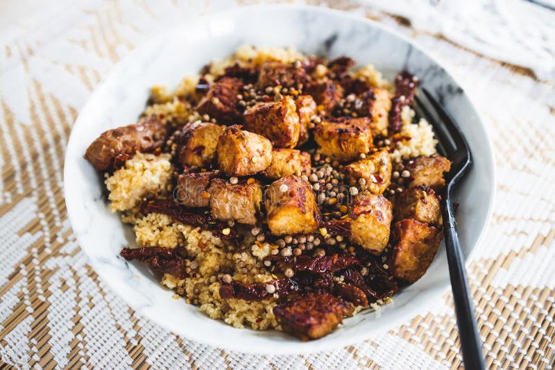 Plant-based couscous with grilled tempeh cubes topped with chilli flkes and coiander seeds stock image Plant-based couscous with grilled tempeh cubes topped with chilli flkes and coiander seeds stock image