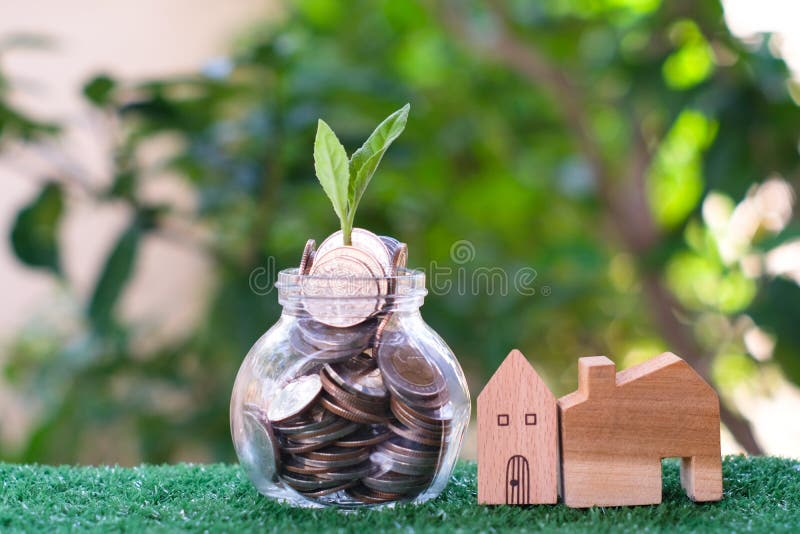 Plant growing from coins in glass jar. Wooden house model on artificial grass. Home mortgage and property investment concept royalty free stock image Plant growing from coins in glass jar. Wooden house model on artificial grass. Home mortgage and property investment concept royalty free stock image