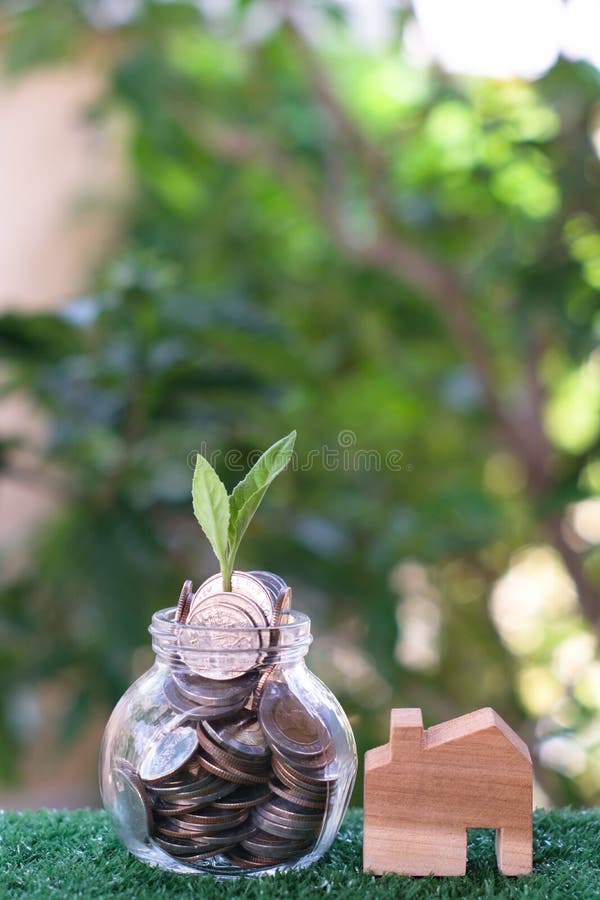 Plant growing from coins in glass jar. Wooden house model on artificial grass. Home mortgage and property investment concept royalty free stock photos Plant growing from coins in glass jar. Wooden house model on artificial grass. Home mortgage and property investment concept royalty free stock photos