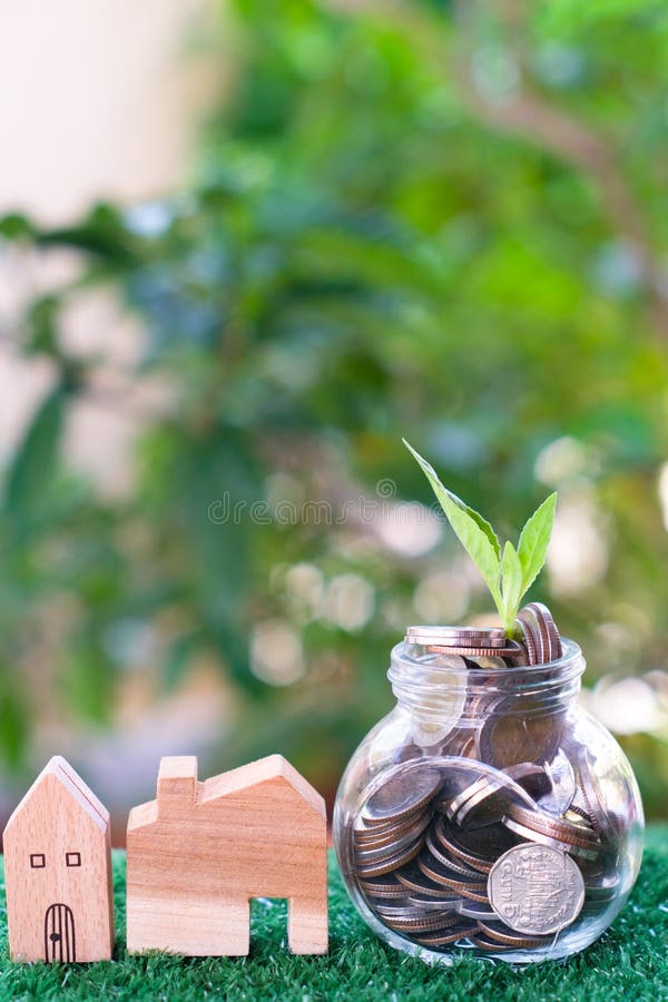 Plant growing from coins in glass jar. Wooden house model on artificial grass. Home mortgage and property investment concept royalty free stock photography Plant growing from coins in glass jar. Wooden house model on artificial grass. Home mortgage and property investment concept royalty free stock photography