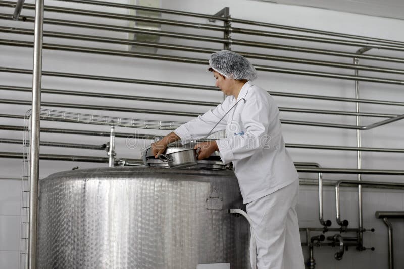 A woman employee is checking the milk from an industrial liquid storage tank in a dairy food production plant. A woman employee is checking the milk from an industrial liquid storage tank in a dairy food production plant