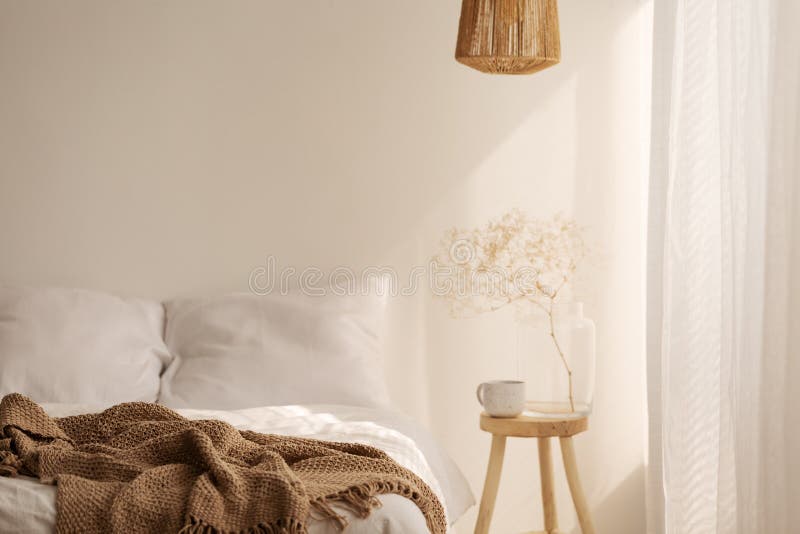 Planta en taburete de madera al lado de la cama con la manta marrón en el interior simple blanco del dormitorio imágenes de archivo libres de regalías Planta en taburete de madera al lado de la cama con la manta marrón en el interior simple blanco del dormitorio imágenes de archivo libres de regalías