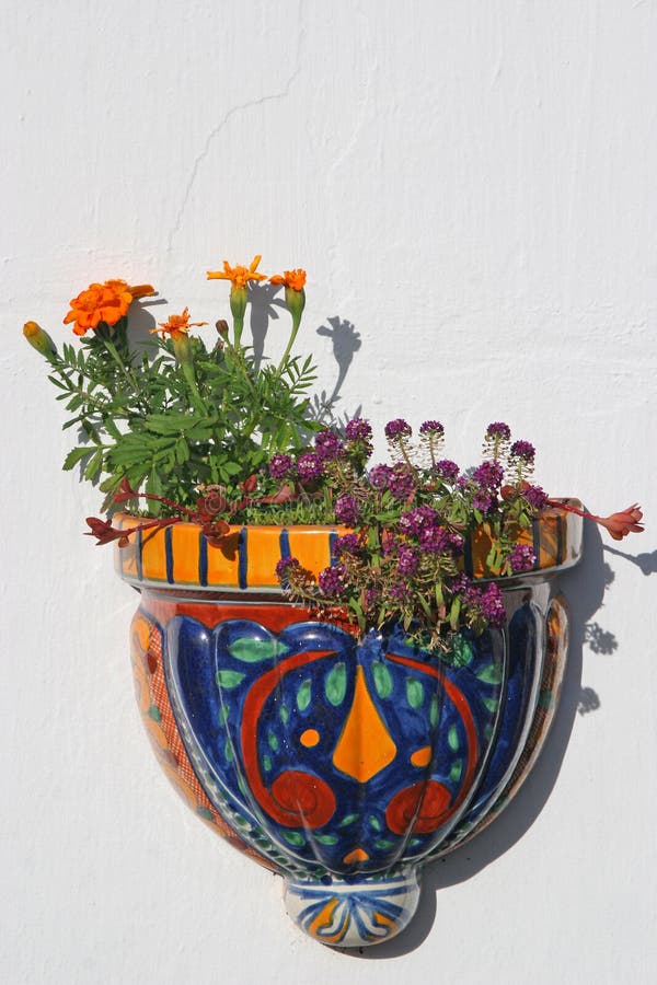 A stucco wall decorated with a glazed ceramic planter filled with marigolds and purple alysum. A stucco wall decorated with a glazed ceramic planter filled with marigolds and purple alysum.