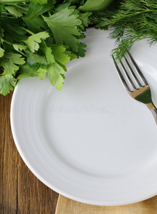 Empty white plate with fork on wooden table with parsley and dill. Empty white plate with fork on wooden table with parsley and dill
