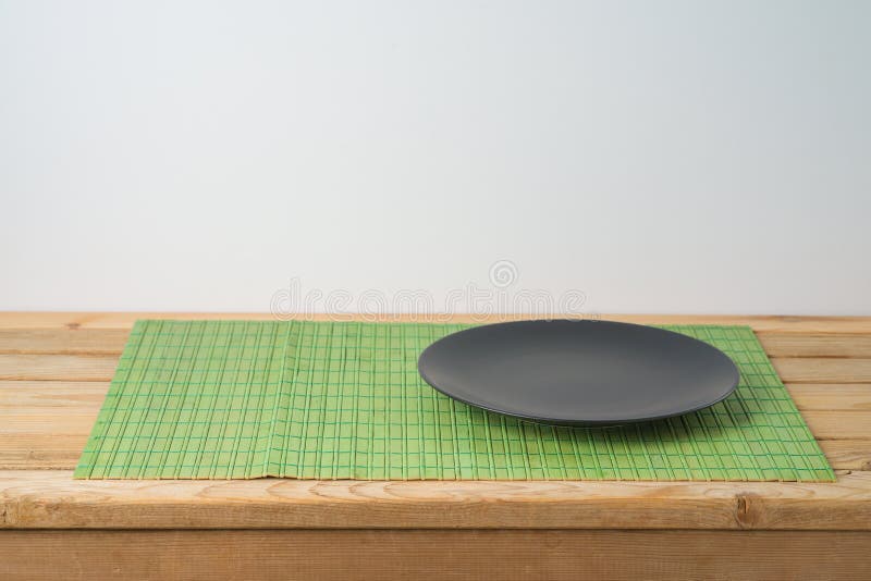 Black  empty plate and bamboo placemat on wooden table. Chinese kitchen or restautant concept background. Black  empty plate and bamboo placemat on wooden table. Chinese kitchen or restautant concept background