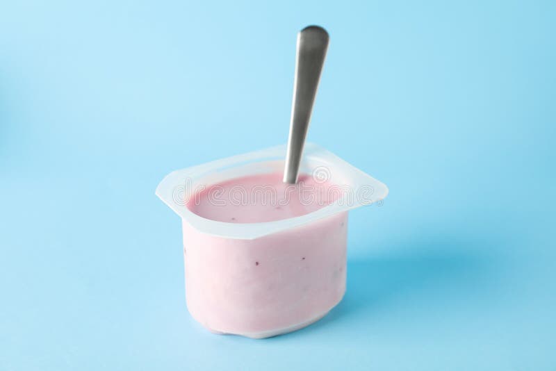 Plast- kopp med yoghurt och sked på färgbakgrund arkivbilder Plast- kopp med yoghurt och sked på färgbakgrund arkivbilder