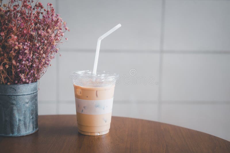 iced latte with straw in plastic cup on wood table in coffee shop