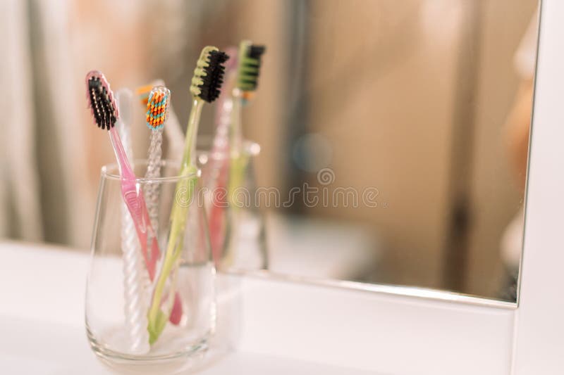 Plastic Different Toothbrushes in Glass Cup in Front of Mirror Stock