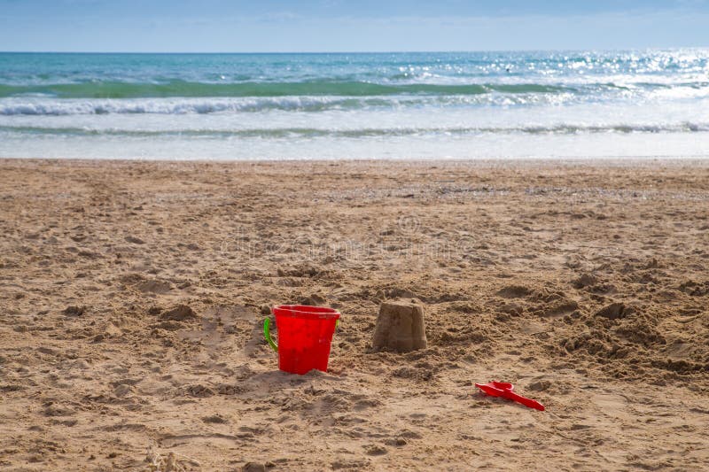 A plastic red bucket lies on the sand of an empty beach