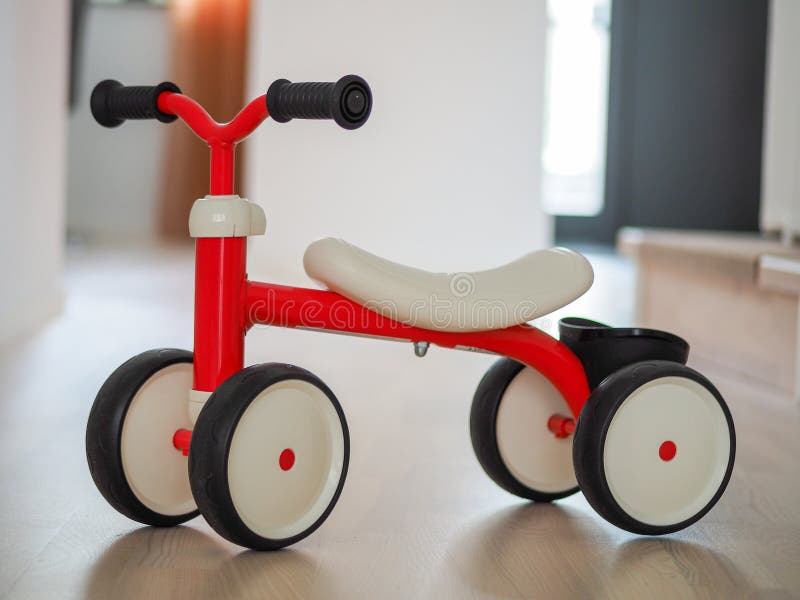 Plastic Red Four Wheeled Child Bicycle on the Wooden Floor Stock Photo