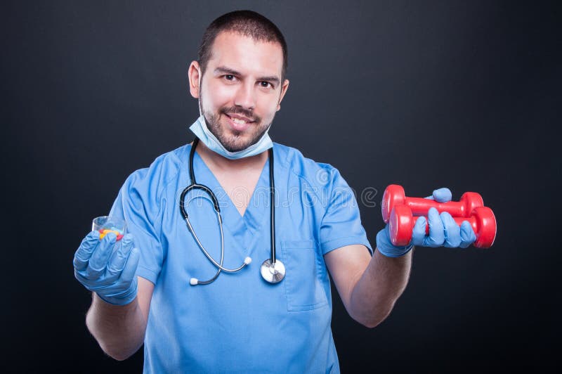 Plastic surgeon wearing scrubs holding dumbbell and pills royalty free stock photography