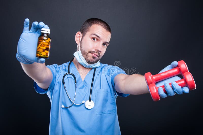 Plastic surgeon wearing scrubs showing dumbbells and pills royalty free stock photography