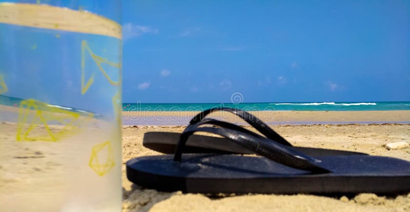 Closeup of Water Bottle and Black Flip Flops on a Beach Stock Image