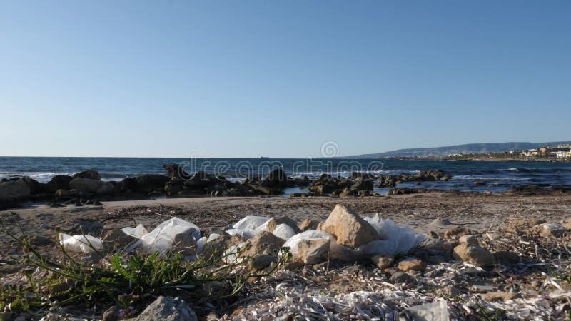 Plastic zakken en document afval op het zandige vuile strand Overzeese golven die het strand op de achtergrond raken