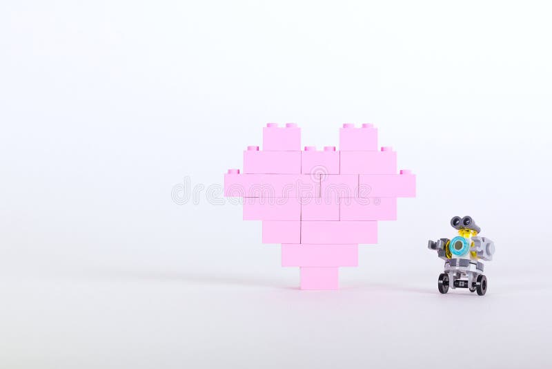 Plastkonstruktorns tegel i form av rosa hjärta med liten robot Vit bakgrund royaltyfri bild