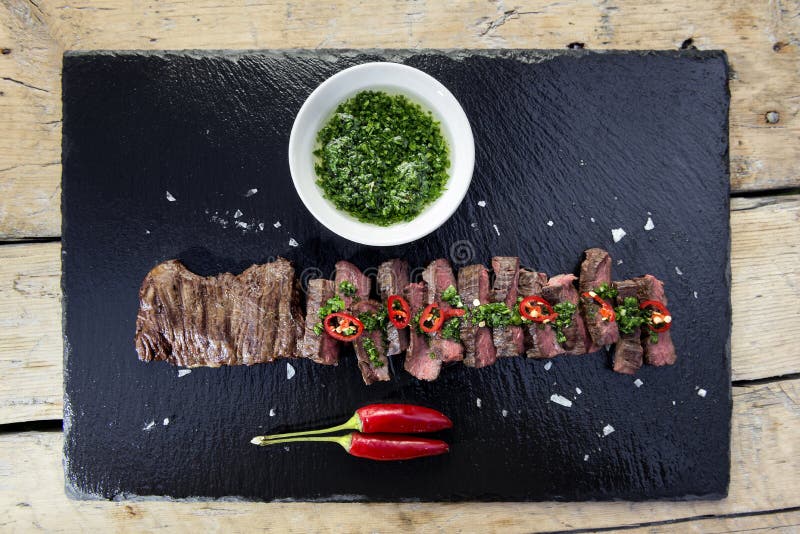 Plat en pierre noir avec le poivre de bifteck de jupe et la sauce à chimichurri image libre de droits Plat en pierre noir avec le poivre de bifteck de jupe et la sauce à chimichurri image libre de droits