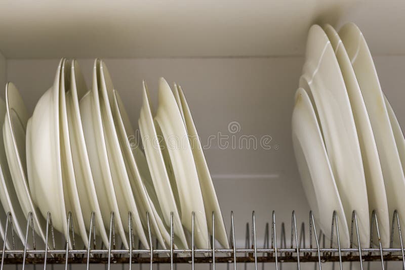 Plat séchant le support en métal avec de grands plats propres blancs et jaune-clair intéressants sur le fond brouillé Cuisine con image stock Plat séchant le support en métal avec de grands plats propres blancs et jaune-clair intéressants sur le fond brouillé Cuisine con image stock