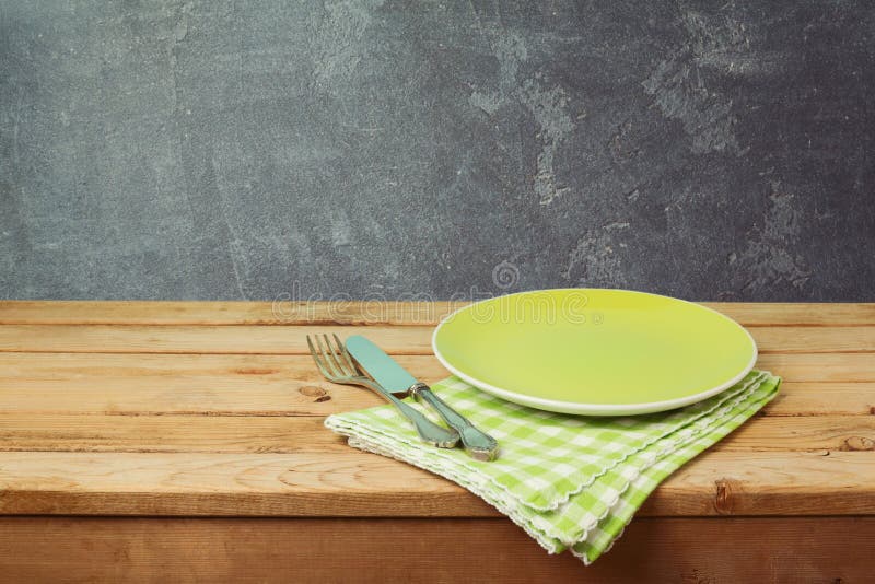 Green plate on wooden table over blackboard background. Dinner setting concept. Green plate on wooden table over blackboard background. Dinner setting concept