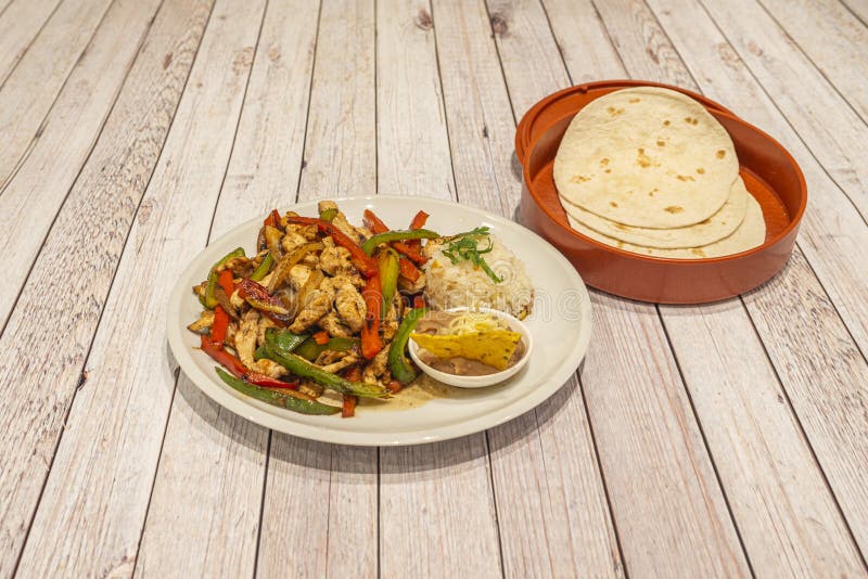 Plate of chicken fajitas with sautÃ©ed red and green peppers, onion, white rice and cheese with bowl of wheat tortillas to make