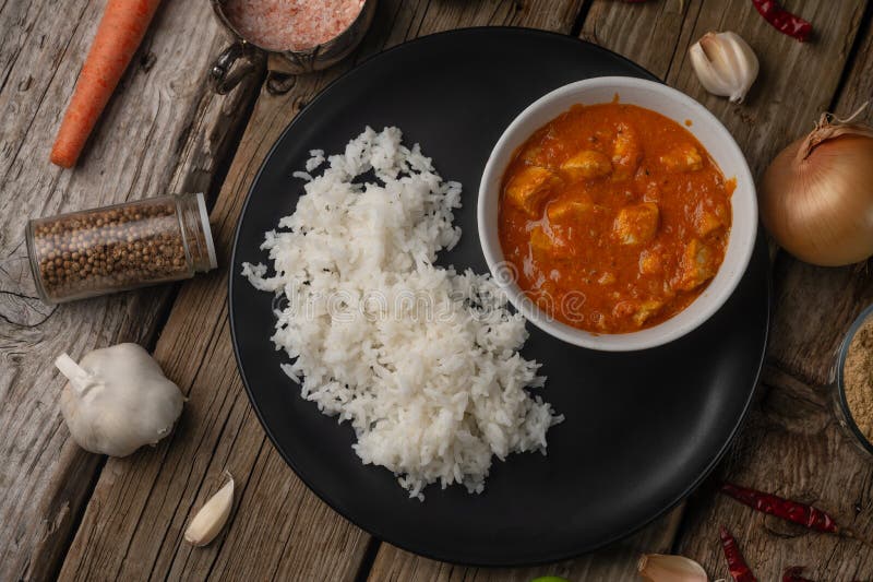 Plate with classic chicken curry and rice served with lime and spices on rustic wooden table background. Traditional indian cuisine. Asian recipe..