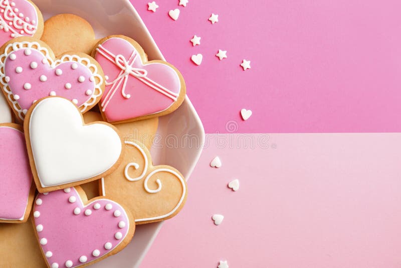 Plate with decorated heart shaped cookies and candy confetti on color background, top view.