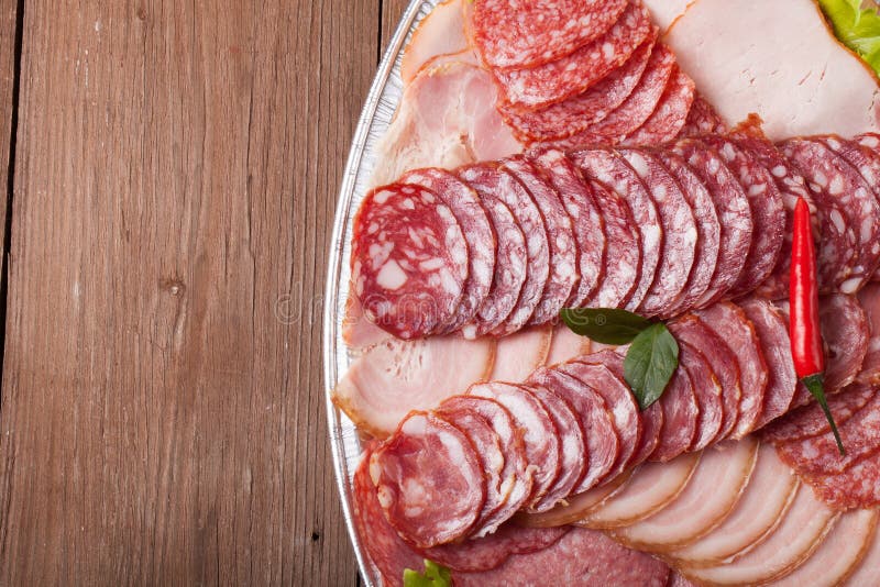 Plate with different sliced sausage on an old wooden table. With