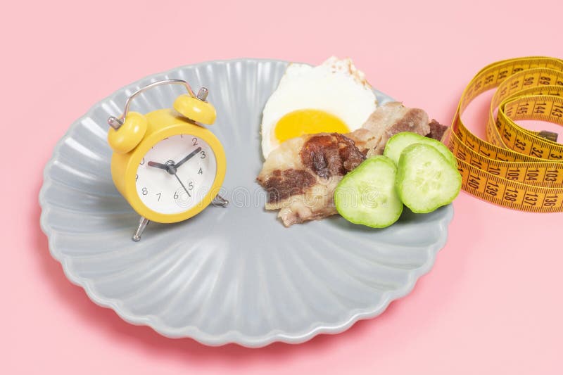 Plate with food and alarm clock on pink background, intermittent fasting concept. royalty free stock images