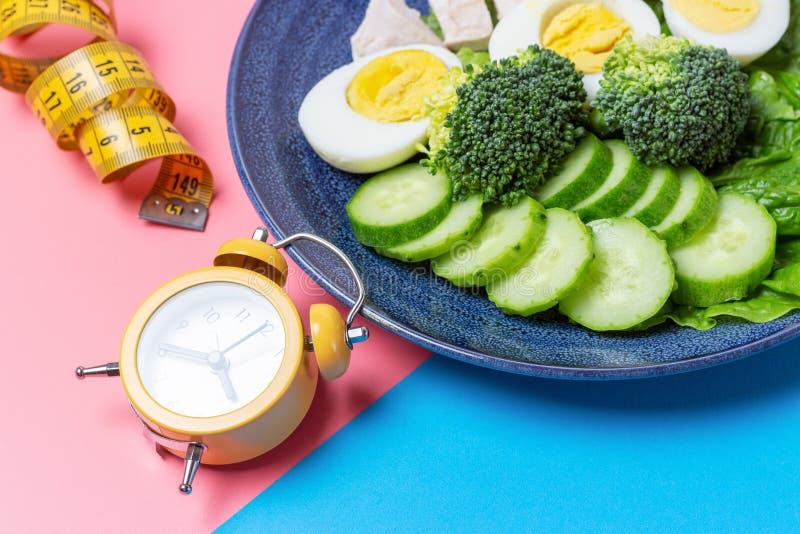 Plate with food and alarm clock on pink and blue background royalty free stock image