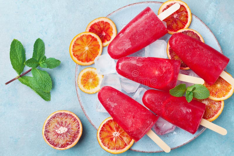 Plate with homemade citrus ice cream or popsicles decorated mint leaves and orange slices on table top view. Frozen fruit juice.