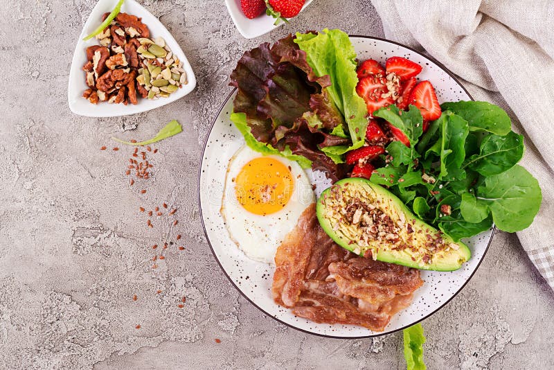 Plate with a keto diet food. Fried egg, bacon, avocado, arugula and strawberries.