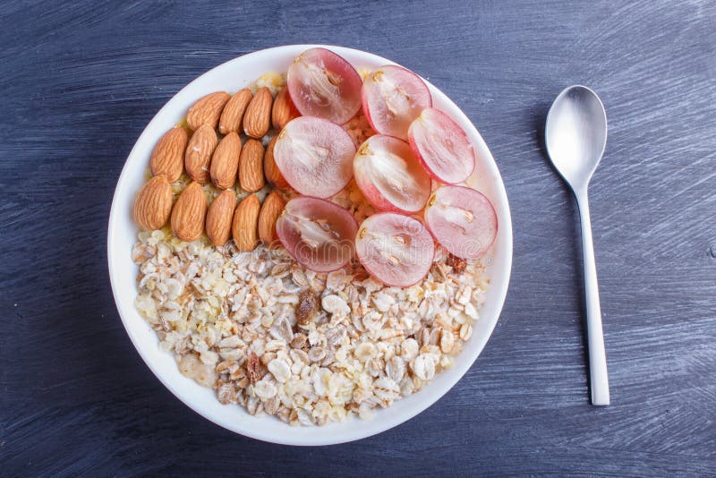 A plate with muesli, almonds, pink grapes on a black wooden background royalty free stock image A plate with muesli, almonds, pink grapes on a black wooden background royalty free stock image