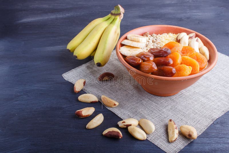 A plate with muesli, banana, dried apricots, dates, Brazil nuts on a black wooden background stock images A plate with muesli, banana, dried apricots, dates, Brazil nuts on a black wooden background stock images