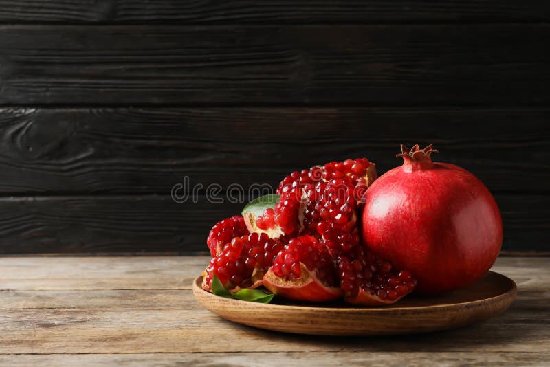 Plate with ripe pomegranates on wooden table against dark background