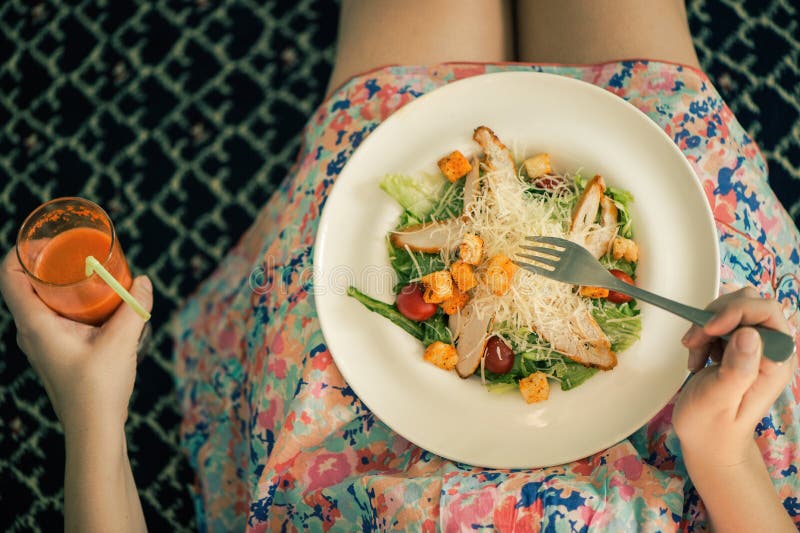 A plate with a salad on female knees and glass of carrot juice. View from above. The concept of food and healthy lifestyles.